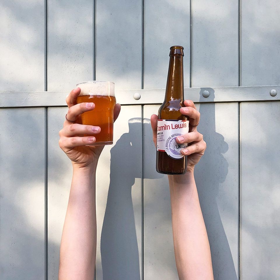 Two hands hold up a glass of beer and a bottle of the Camin Lewis beer