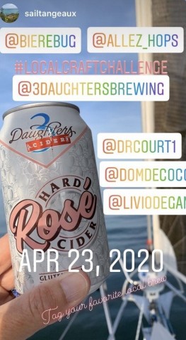 A hand holds up a can of hard cider, in the background we see a sail boat at sea